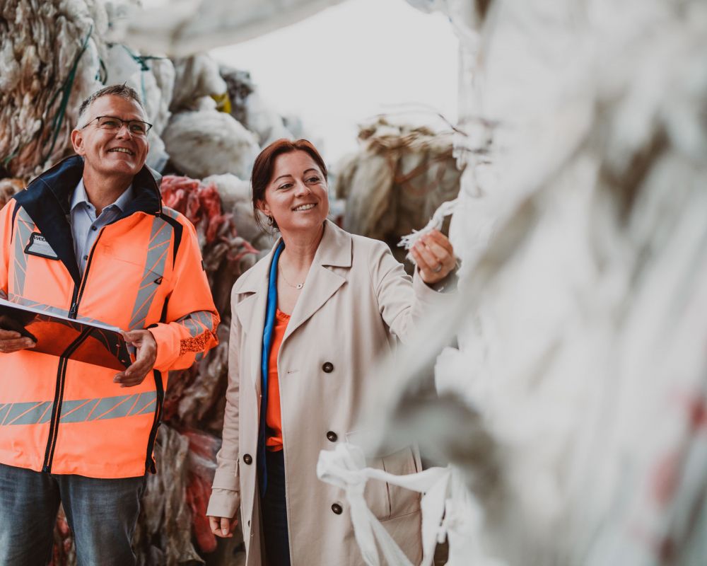 Ein freundlicher Mann und eine lachende Frau vom Weber Team stehen zwischen gepressten Folien und Kartonagen und prüfen in ihrer Hand die Materialien.