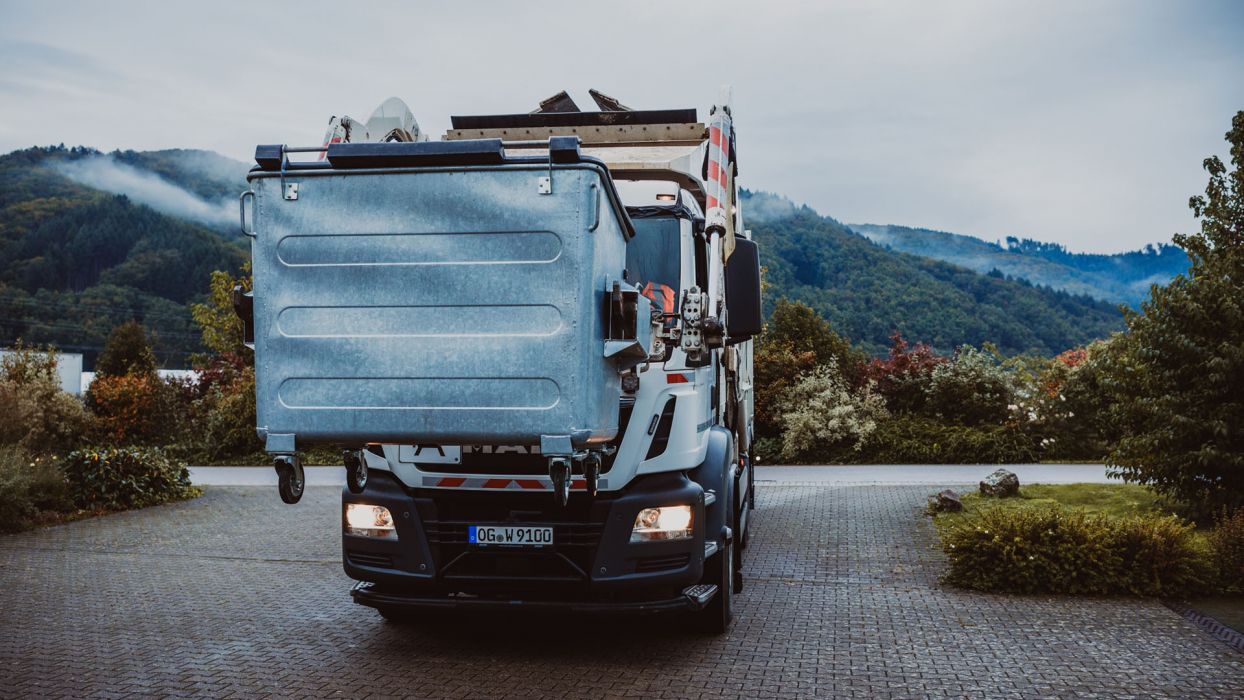Weber LKW Frontlader hebt Umleerbehälter hoch. Im Hintergrund der Schwarzwald.