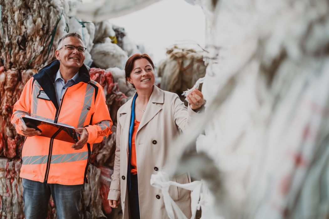 Ein freundlicher Mann und eine lachende Frau vom Weber Team stehen zwischen gepressten Folien und Kartonagen und prüfen in ihrer Hand die Materialien.