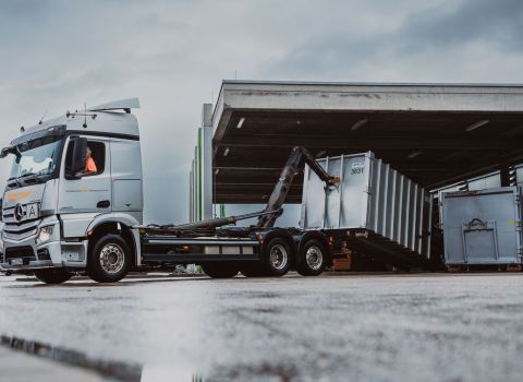 Weber LKW steht auf einem Hof und lädt unter einem Dach einen Abrollcontainer ab.